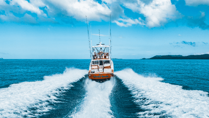 Image of Chino Salsa Fishing charter boat racing across bright blue ocean water, leaving a wide white wake behind it under a sunny, partly cloudy sky.