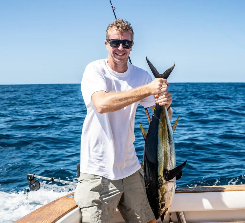 Image of a happy Chino Salsa's customer holding his big game catch onboard Chino Salsa's boat on a sunny day wearing sunglasses and white tshirt.
